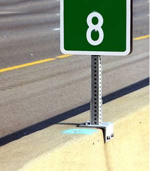 A piece of galvanized square sign post is bolted down to the concrete roadside.