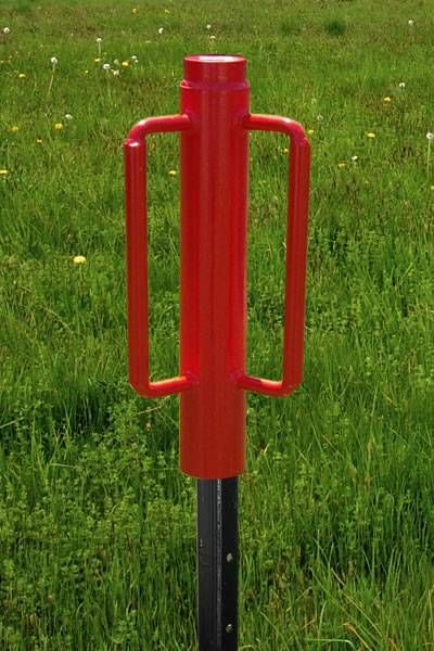 A red post driver is installing a star picket on the grassland with a detail of star picket.