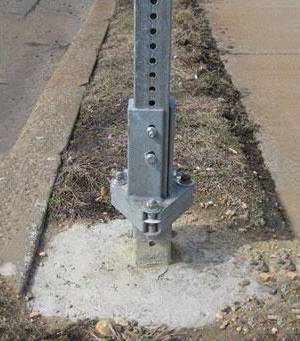 A piece of galvanized square sign post is concreted in the ground.